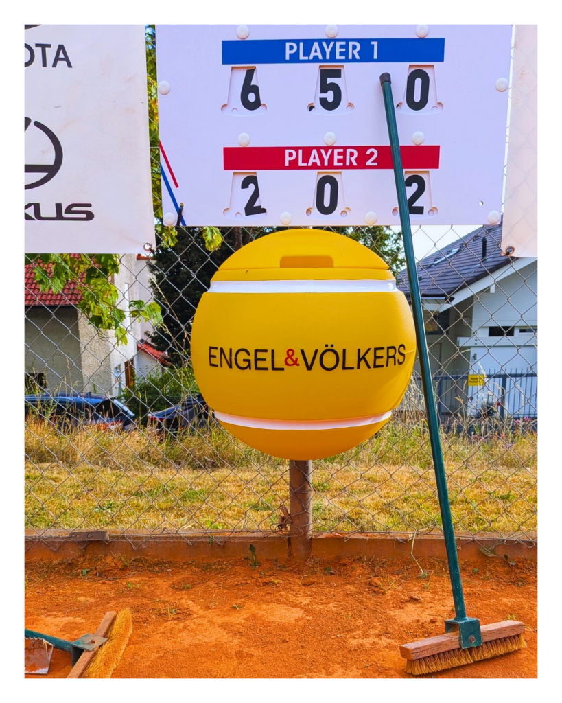 Gelber Tennisball-Mülleimer von Engel & Völkers unter der Spielstandsanzeige